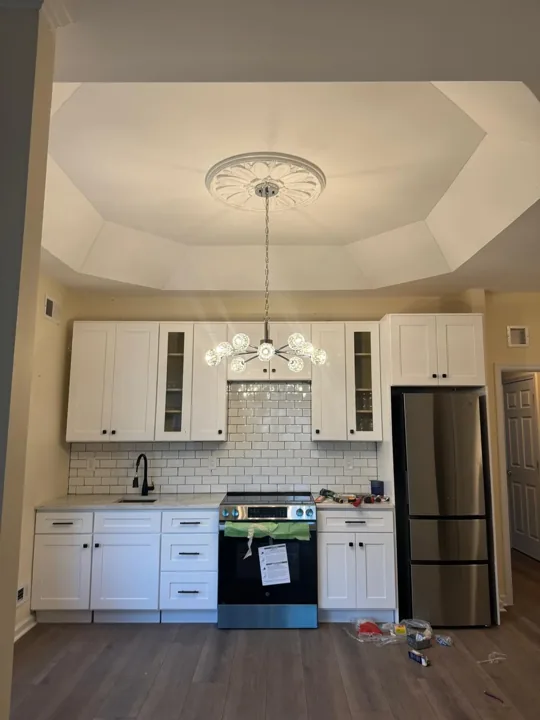Actual kitchen project with white cabinetry, tiled backsplash and installed chandelier; finishing work underway